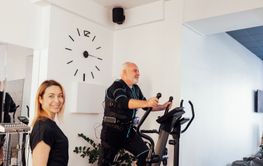 Sports senior grayhaired man is exercising on elliptical...