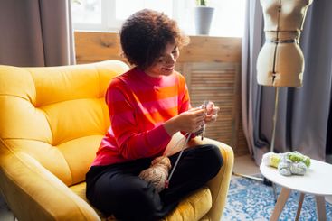 Young African smiles and knits at home in living room....