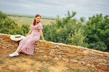 Dreamy young woman is sitting on stone fence.