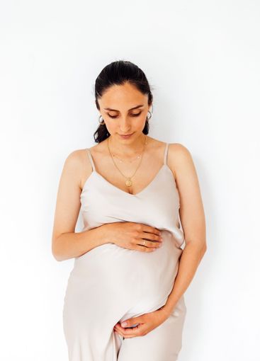 A young pregnant woman stands and gently holds her...