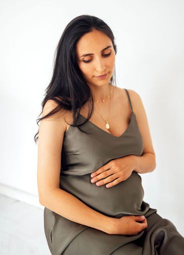 A young pregnant woman sits and gently holds her belly....