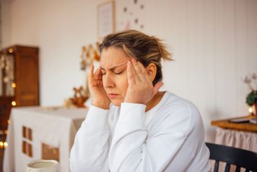 Struggling with a headache, she sits in silence,...