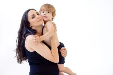 A smiling pregnant woman in a black dress hugs her baby....