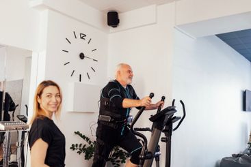Sports senior grayhaired man is exercising on elliptical...