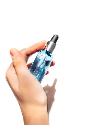hand with a transparent bottle of blue moisturizing serum