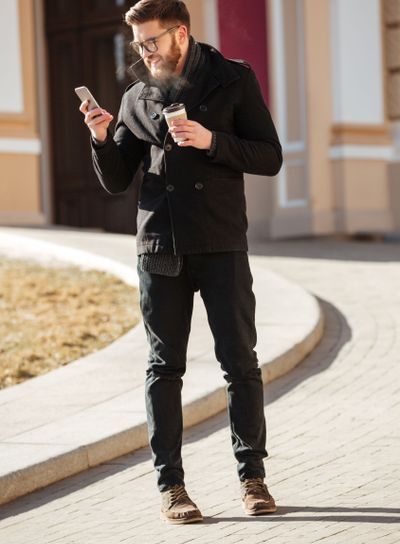 Happy man using cell phone and drinking coffee in city