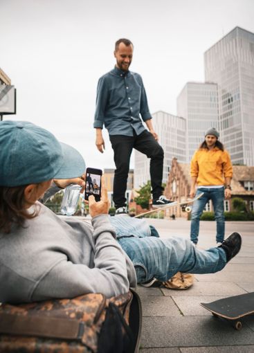 Man photographing while male friend skating on footpath