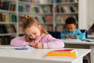 School children sitting at desks in classroom interior,...