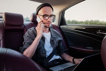 Man with laptop making phone call on a backseat of a car...