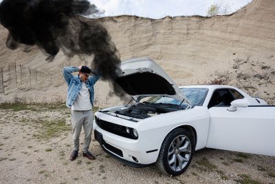 Shocked man is standing near his broken muscle car, open...