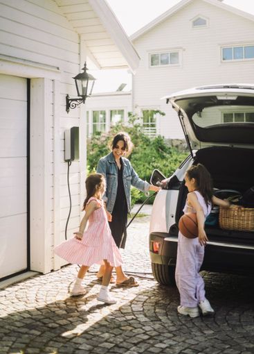 Woman charging electric car while standing with daughters...