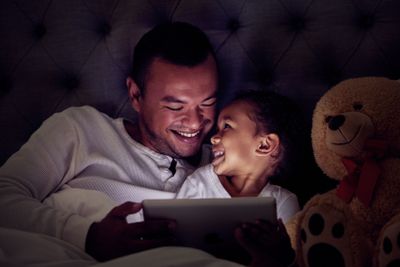 Father and child in bed with tablet reading ebook or to...