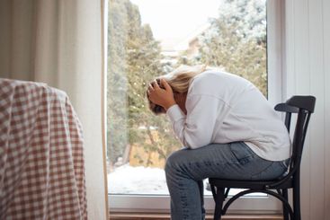 A woman sits by the window, head in hands, embodying a...